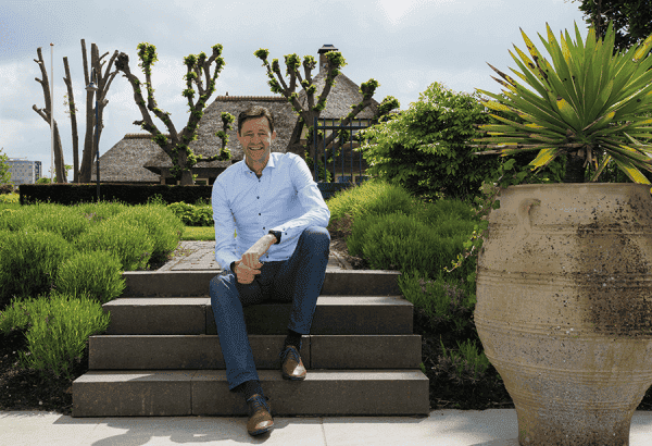 Man zit op tuintrap met groene tuin en grote potplant op achtergrond.