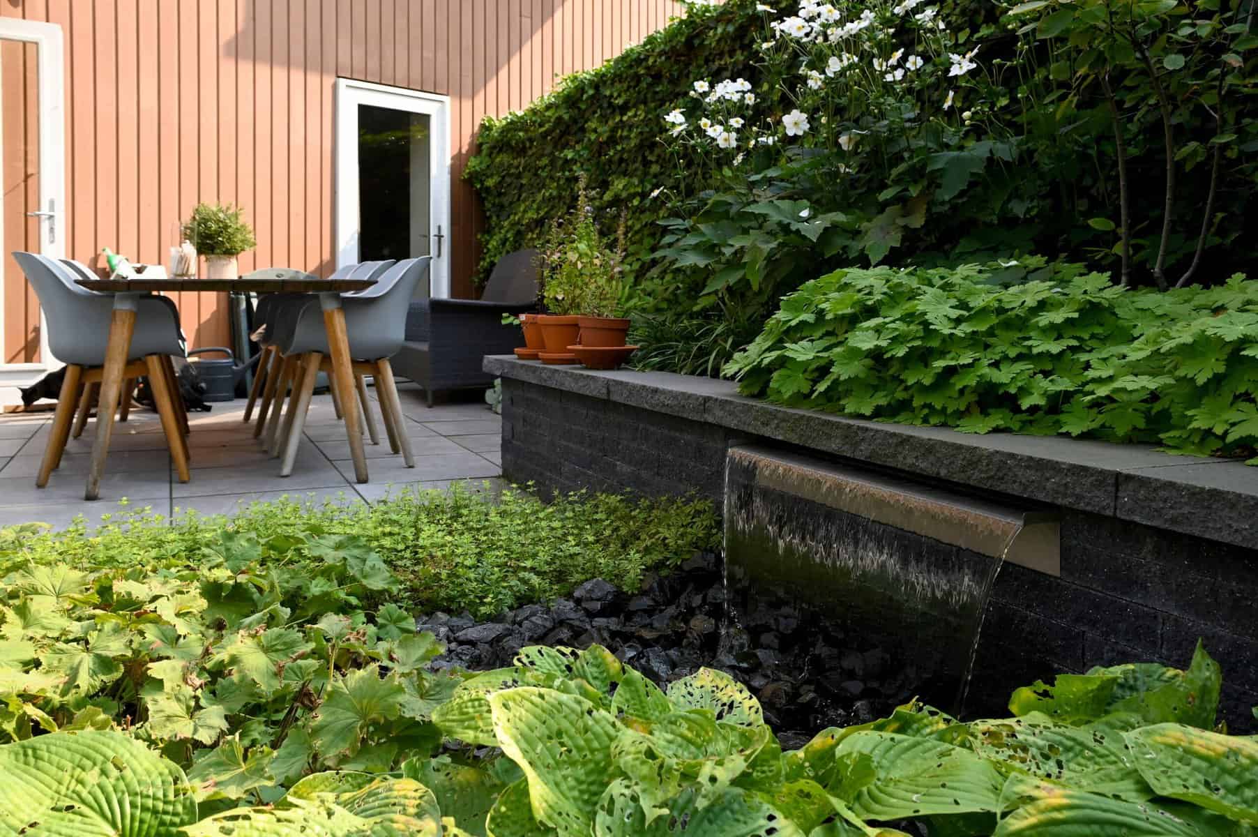Moderne tuin met waterpartij, terras en groene beplanting.