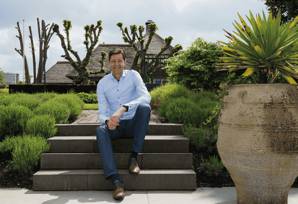 Man zit op trappen in een groene tuin met grote planten en bomen.