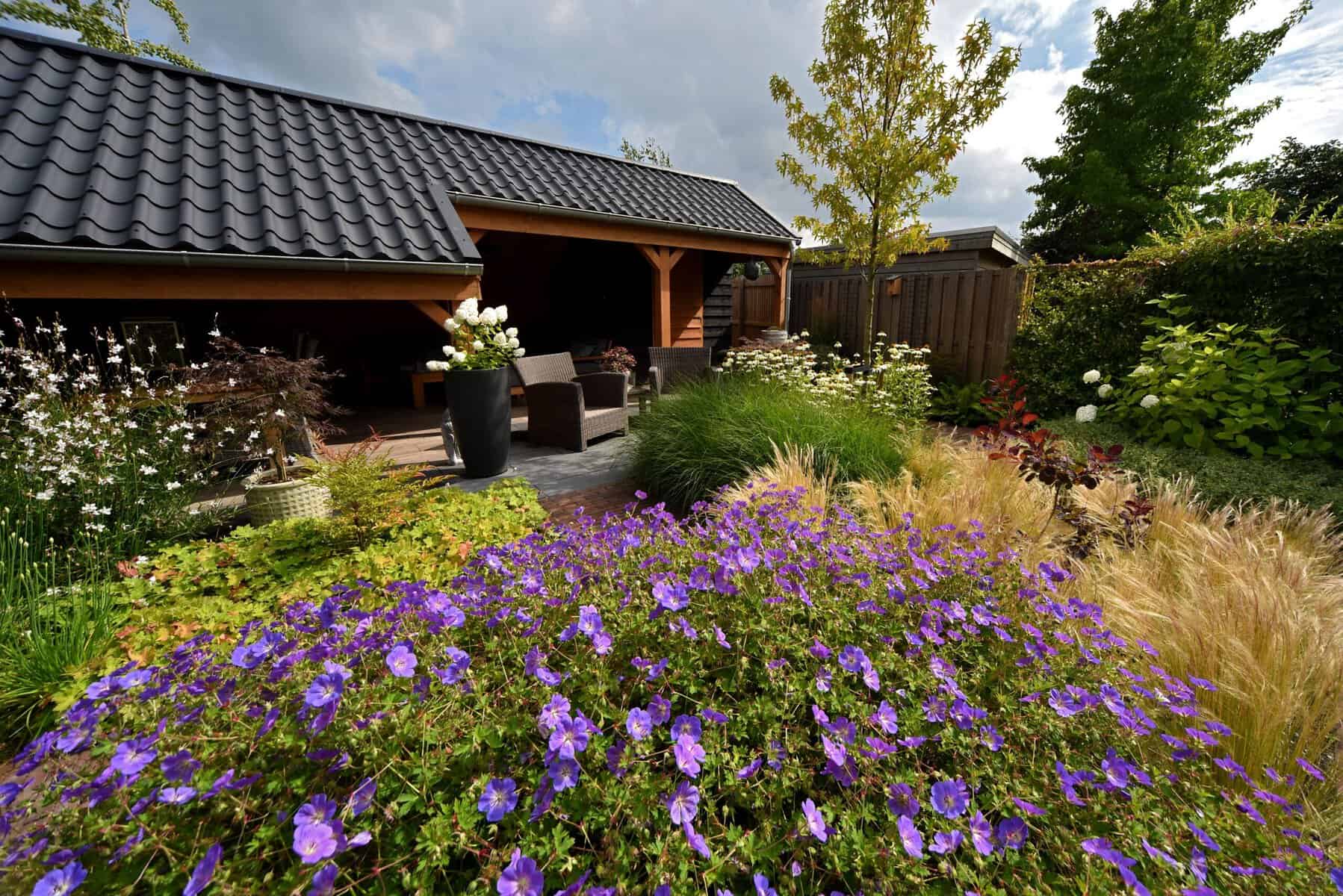 Gezellige tuin met bloemen, terras en schaduwrijke zithoek.