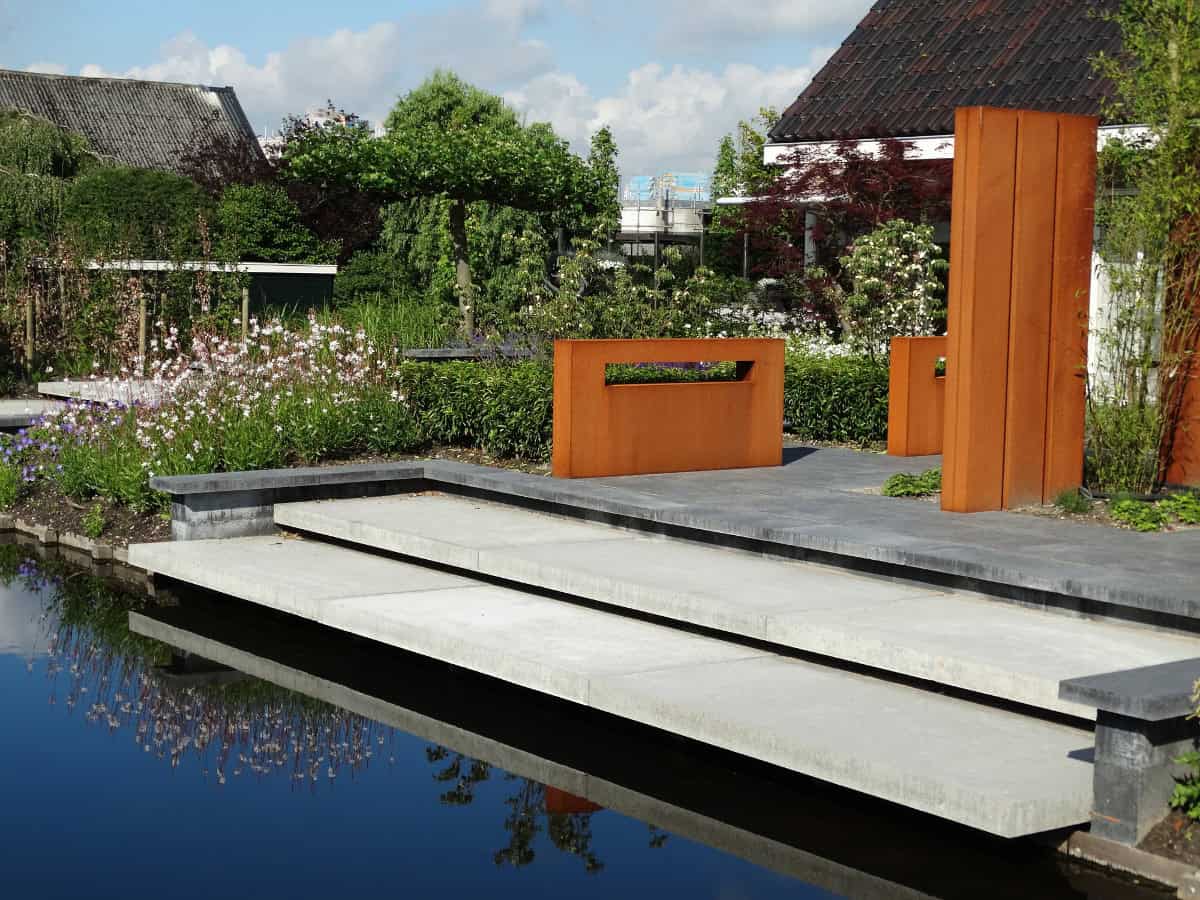 Moderne tuin met terras en waterpartij in een groene omgeving.