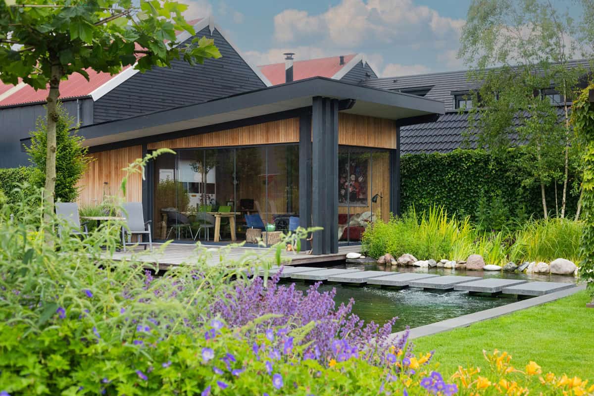 Moderne tuin met vijver, terras en groene beplanting.